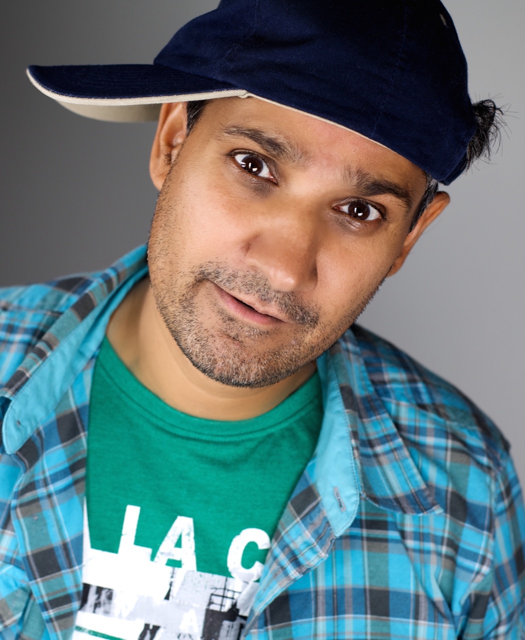 Casual character headshot of Kuldip Korotana wearing a blue cap and plaid shirt